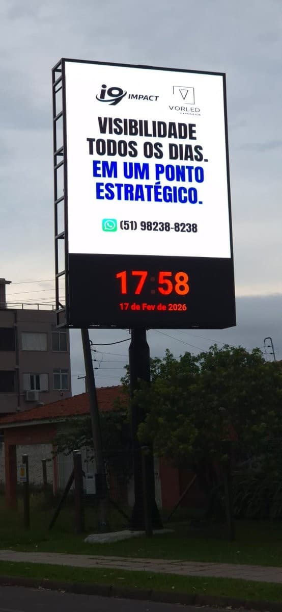 Painel de LED em totem exibindo campanha de visibilidade, contexto urbano ao entardecer.