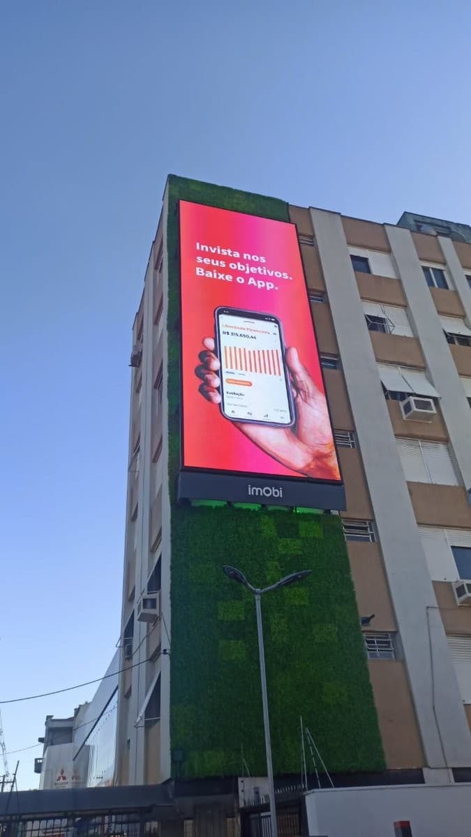 Empena de prédio revestida de LED, painel vertical exibindo campanha, céu azul ao fundo.