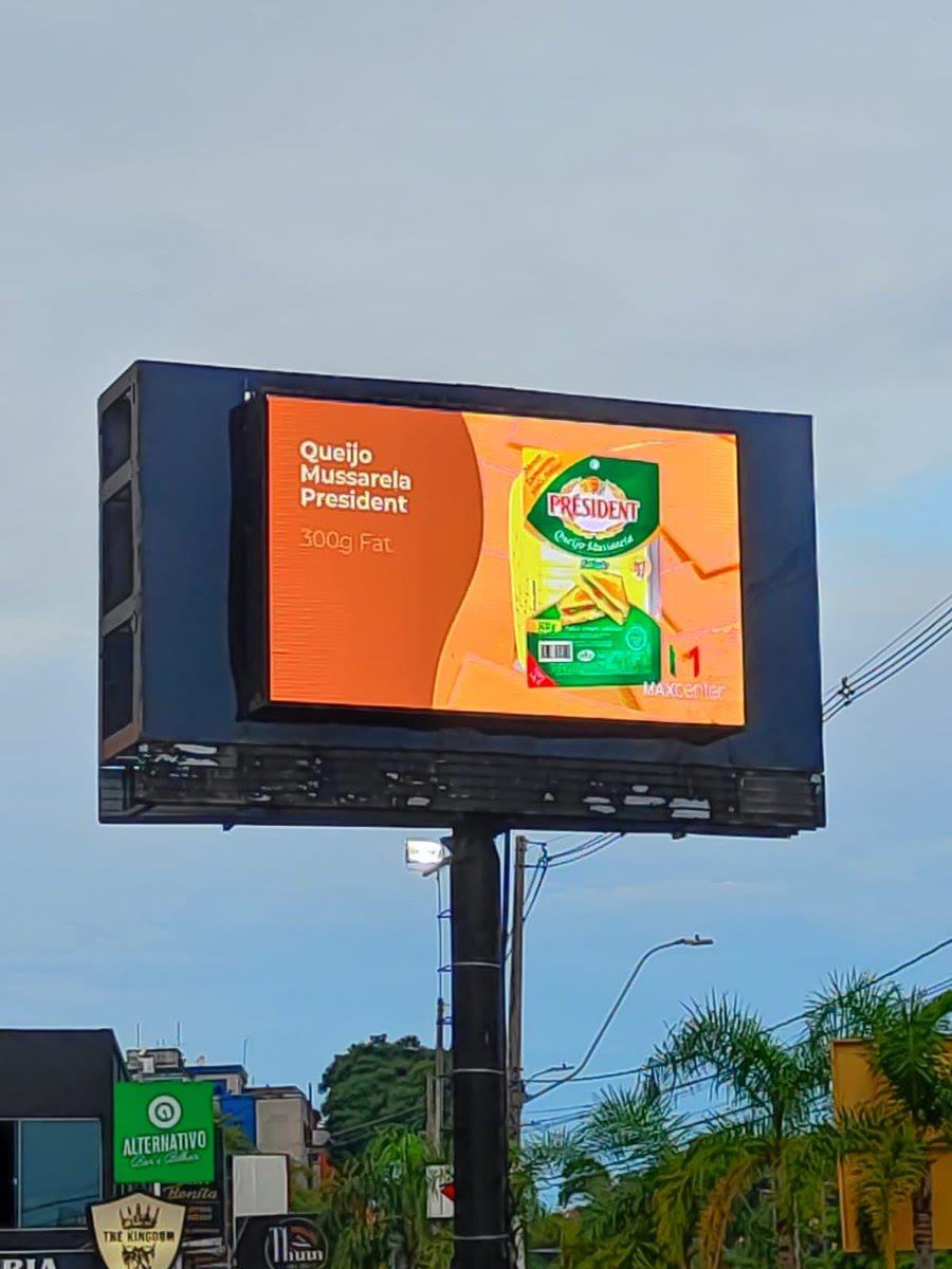 Painel de LED em totem independente, contexto urbano com comércio local ao redor.